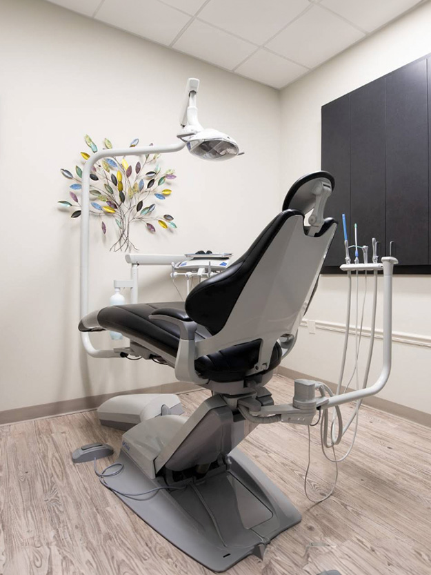 The image shows a dental chair with adjustable controls, situated within a dental office setting, featuring a modern design and a comfortable-looking seat.
