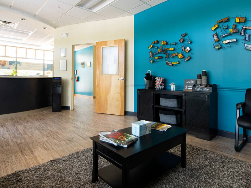 The image shows an interior office space with a colorful wall, a desk, chairs, and a blue carpeted floor.