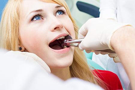 The image shows a woman sitting in a dental chair with her mouth open, receiving dental treatment from a professional who appears to be an oral surgeon or dentist.