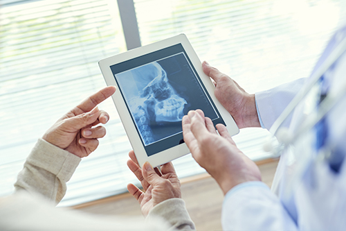 A medical professional is showing an X-ray on a tablet to two individuals while standing in an office setting.