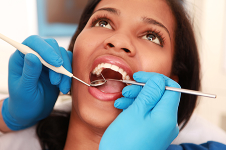 A woman receiving dental care with a hygienist using tools on her teeth.