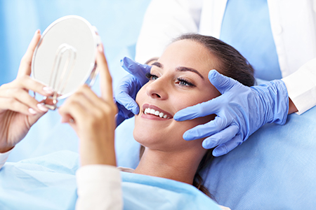 The image shows a person lying on a dental chair with a magnifying mirror held over their face by a professional, likely during a dental examination or procedure.