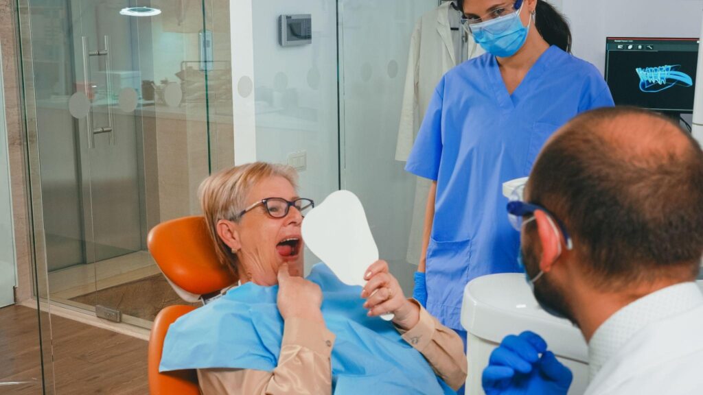 Older woman smiling while checking her teeth in a dental mirror during an appointment with a family dentist in Sarasota.